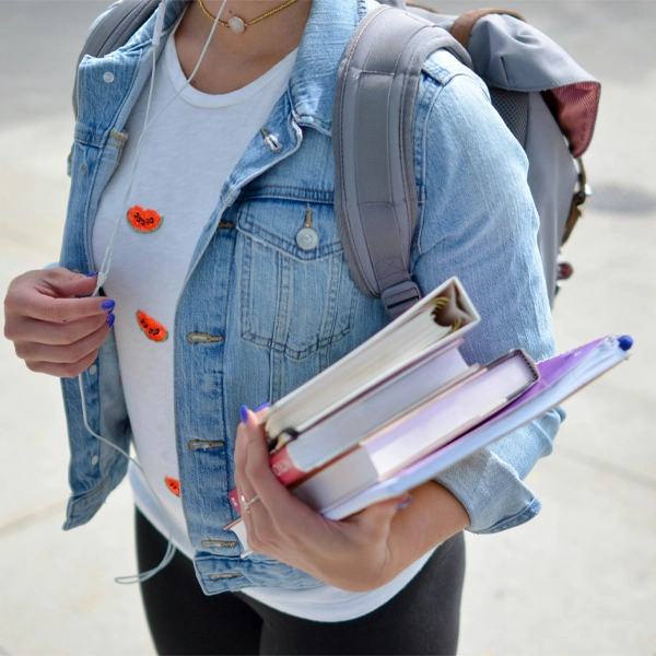 Student carrying books and wearing a backpack, ready for class