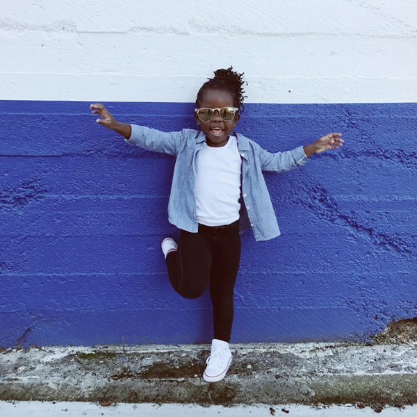 A young child wearing sunglasses and a casual outfit, posing confidently against a blue wall, featured on a poster made with Poster Studio Express poster makers