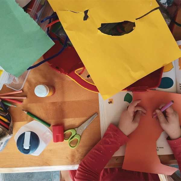 Child working with colored paper, scissors, and art supplies at a desk, creating a poster for classroom learning