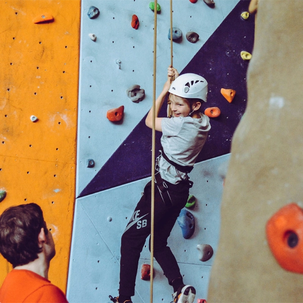 Blog Post 10.9.3 Child rock climbing on an indoor wall during a school event, guided by an instructor